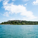 A calm body of water with an island covered in greenery and rocky formations under a partly cloudy sky.