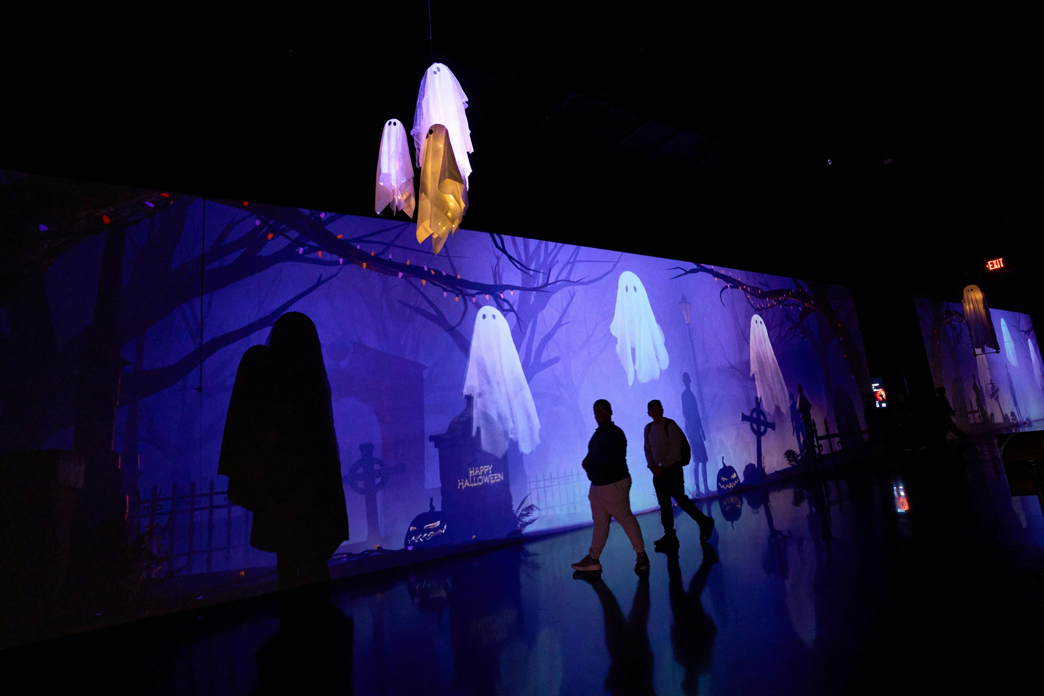 People walking in a dark room with a Halloween-themed display, including floating ghost decorations and a spooky backdrop.