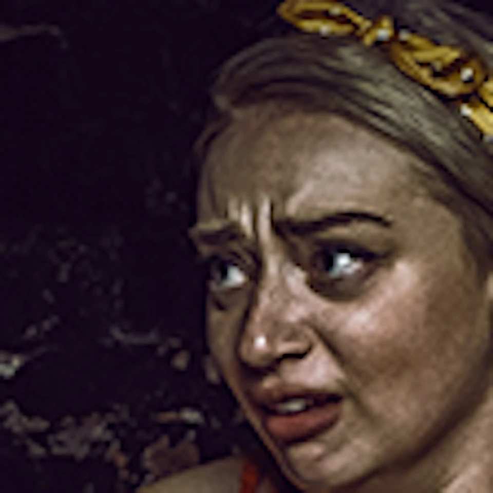 Three people on a bench react with fear and excitement as a person to the left reaches towards them in a dark room.