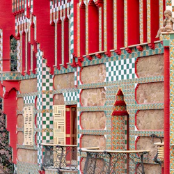 Utsmyckad byggnadsfasad med röda väggar, dekorativa gröna och vita plattor, balkonger i smidesjärn och invecklade geometriska mönster.