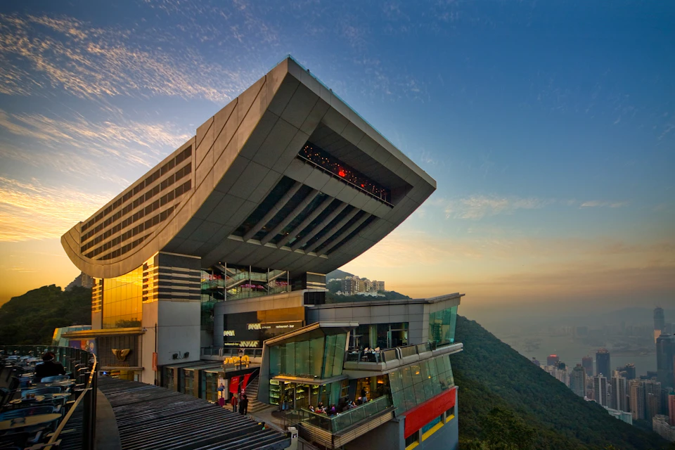 A modern architectural building with a curved rooftop, featuring glass facades and set against a mountain and sunset sky.