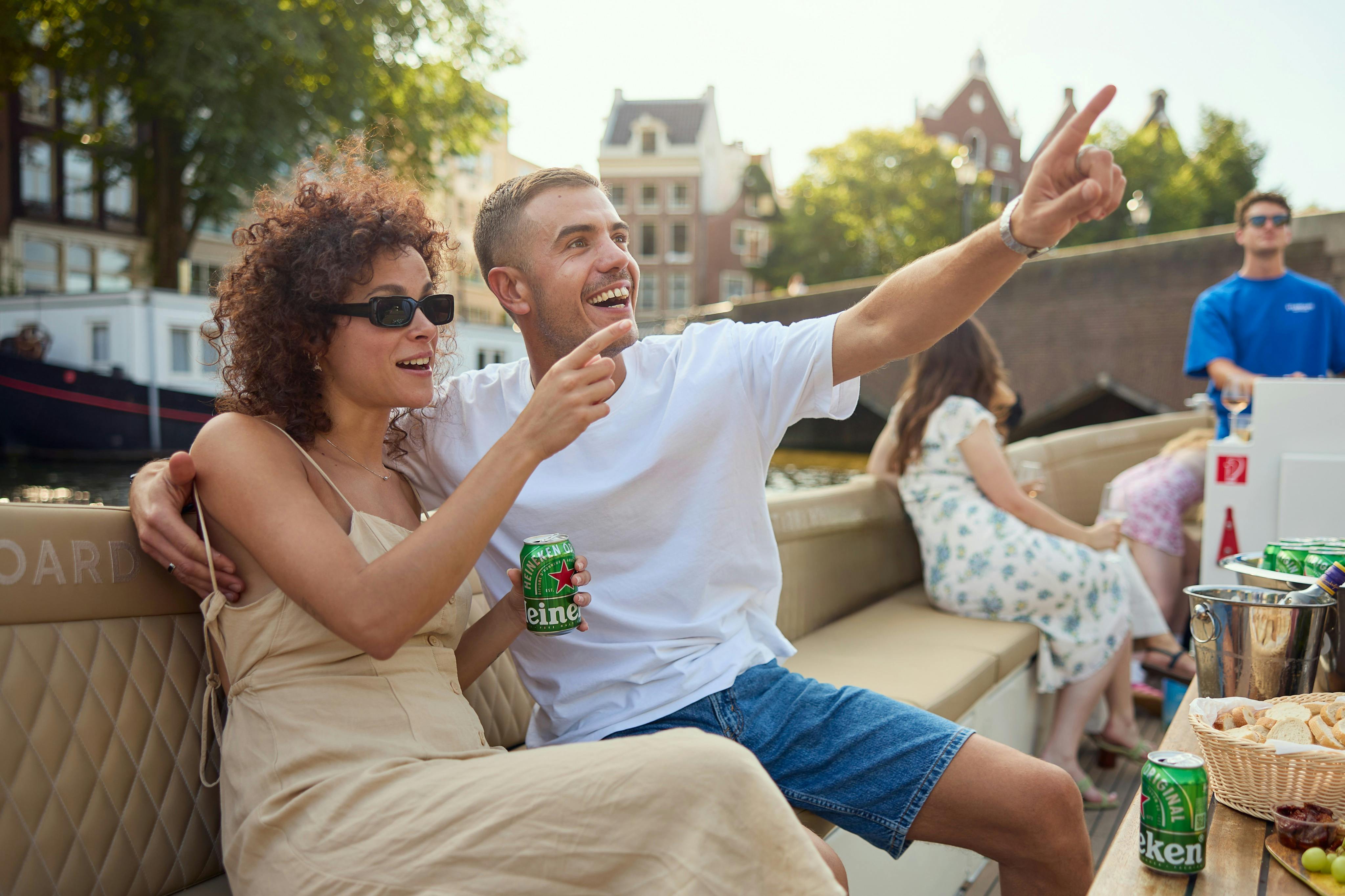 Ett leende par njuter av en båttur en solig dag, med kanalhus och träd synliga i bakgrunden.