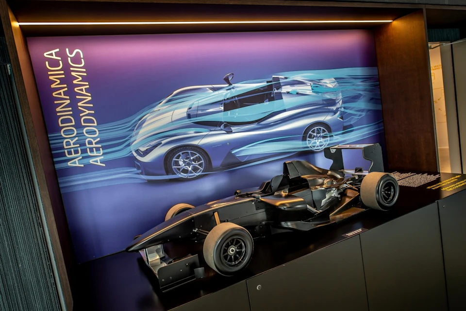 Model of a sleek, black race car displayed in front of an illustration depicting streamlined aerodynamics.