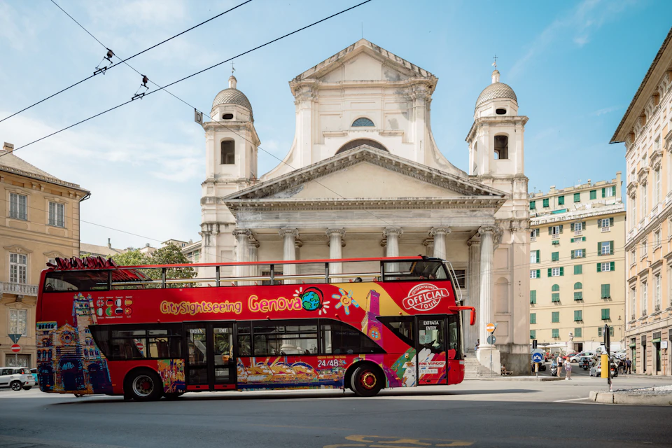 A red sightseeing bus parked in front of a historic church with two bell towers and a blue sky in the background.