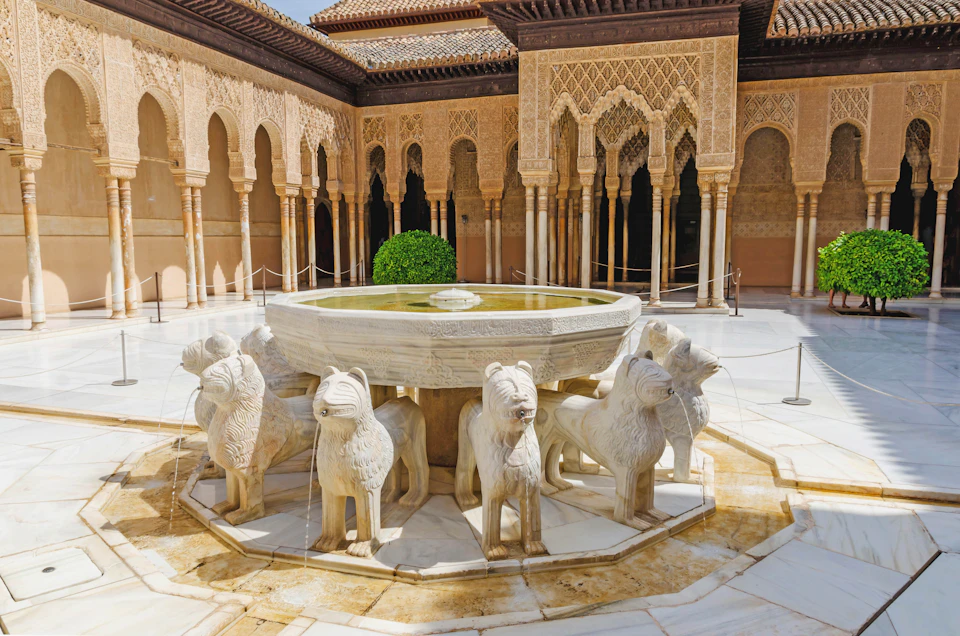 Intricately carved stone lions support a circular fountain in a courtyard surrounded by ornate archways.