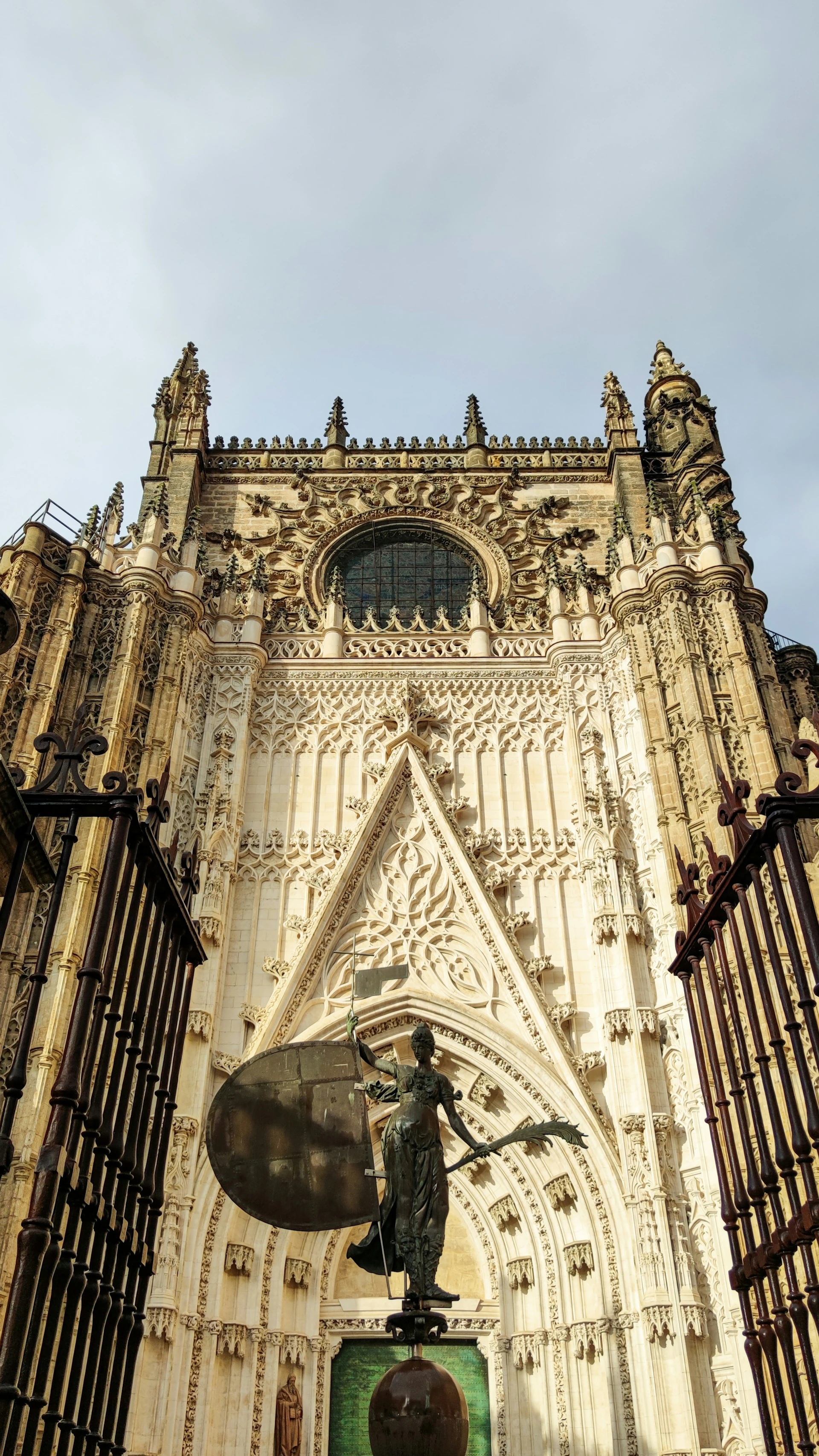 Gothic cathedral facade with detailed carvings, a large circular stained-glass window, and an ornate triangular arch above a statue.