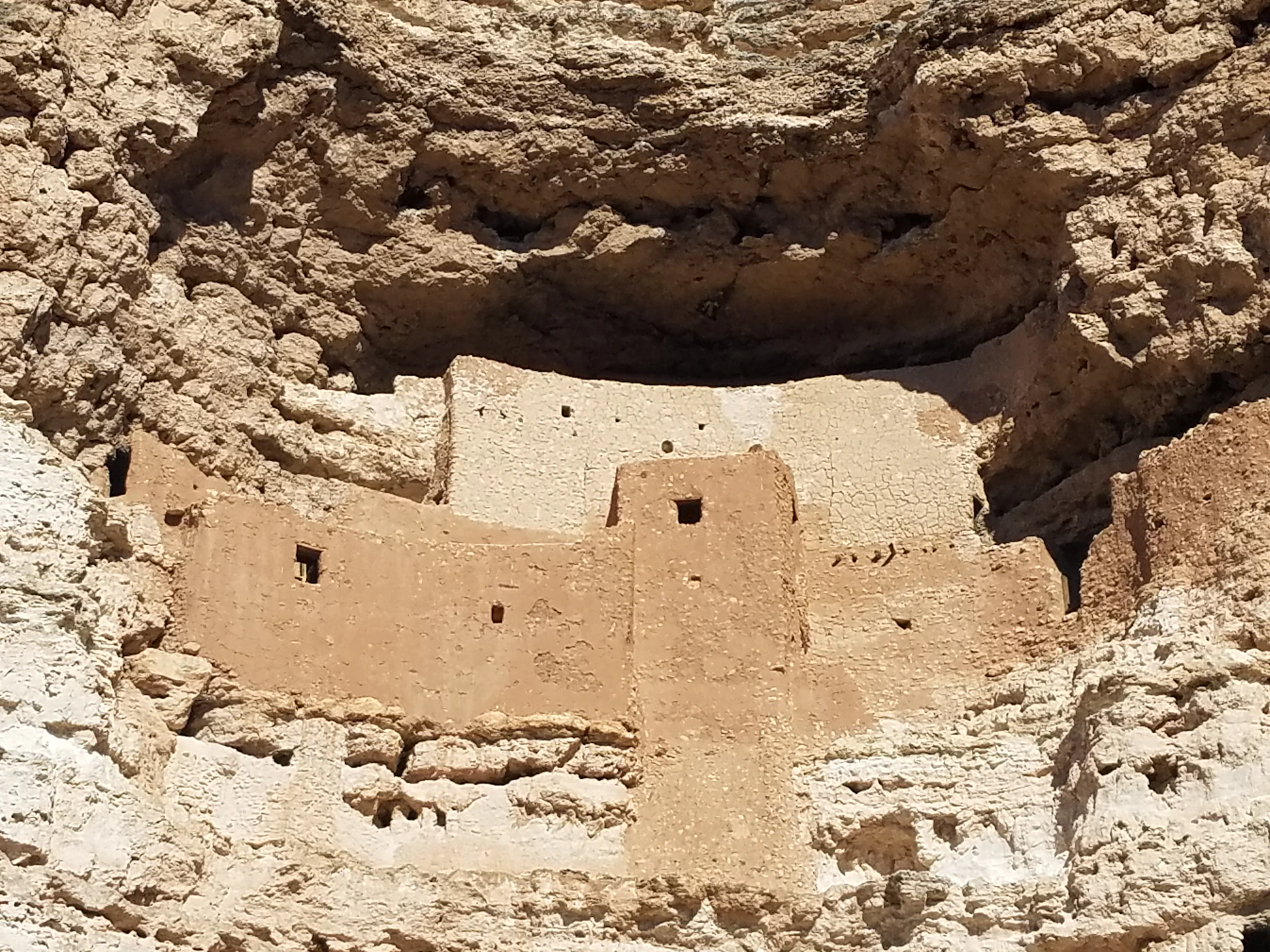 Ancient cliff dwelling built into a rocky cliff face, featuring multiple small windows and a central tower-like structure.