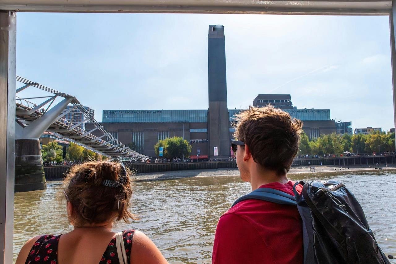 화창한 날씨에 런던의 테이트 모던 (Tate Modern) 과 밀레니엄 브리지 (Millennium Bridge) 의 강변 전망을 감상하는 보트 두 사람.