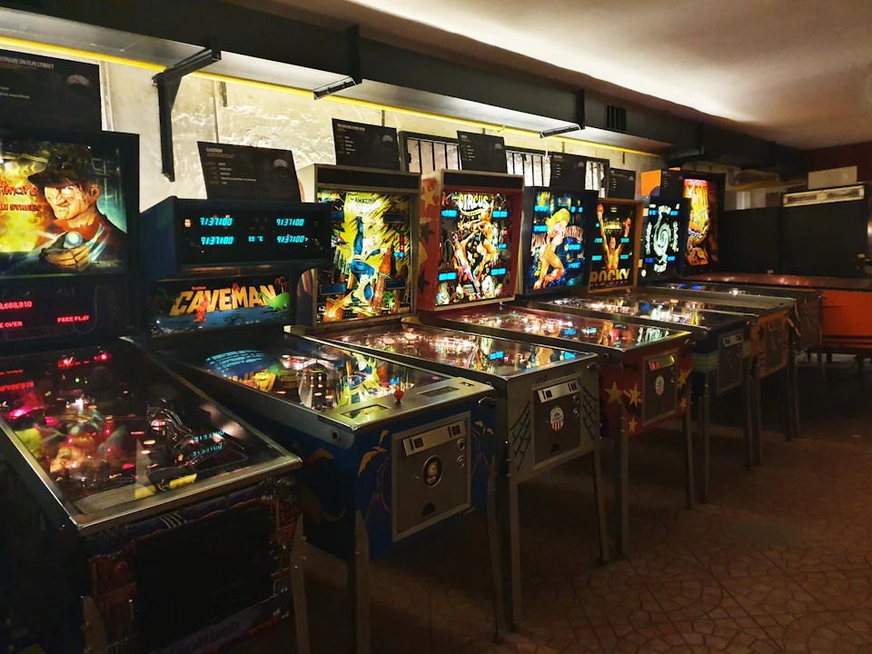 A row of colorful, vintage pinball machines illuminated in a dimly lit arcade setting.