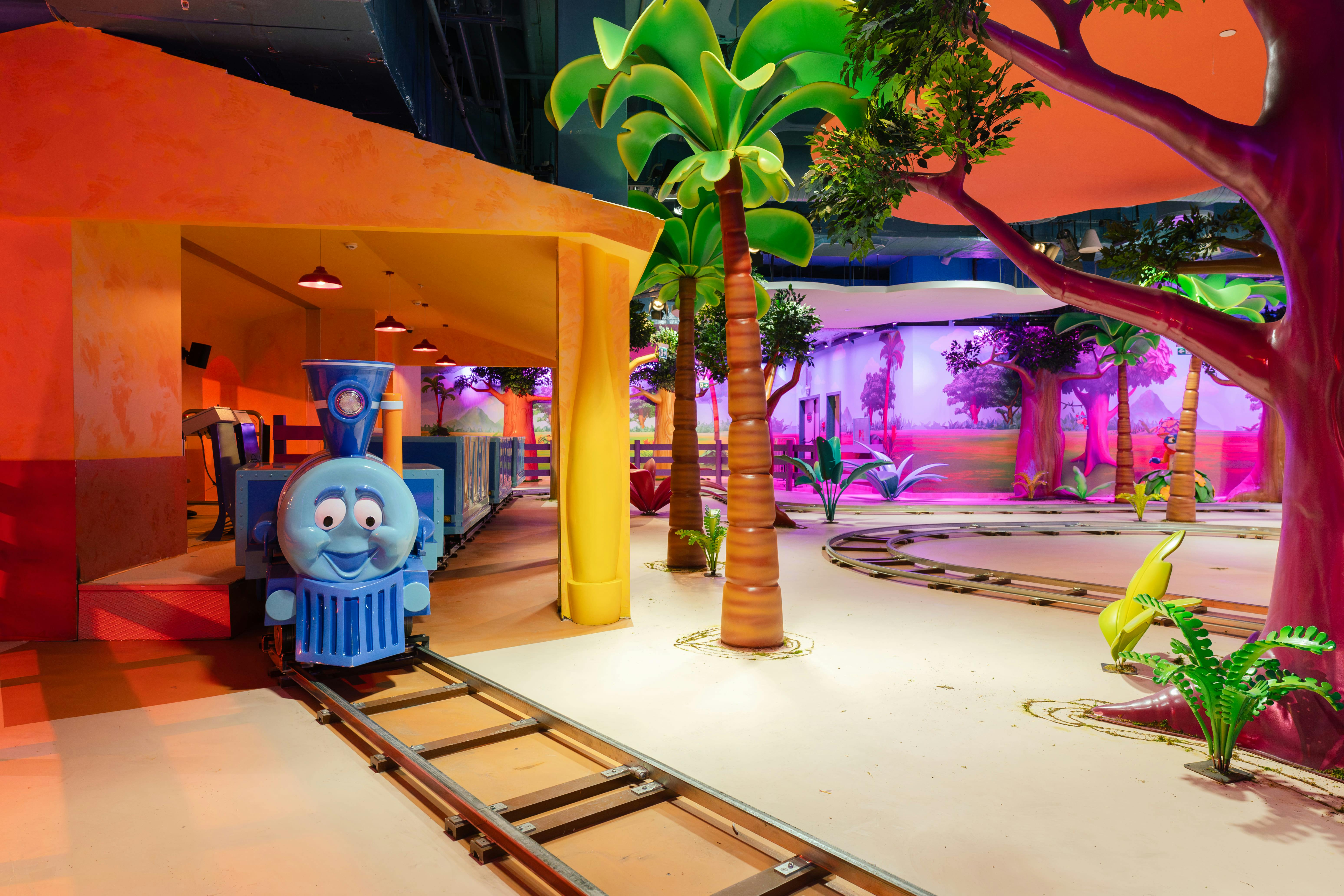 Een grillige indoor treinrit met een blauwe trein met een lachend gezicht, omringd door een kleurrijk tropisch landschap.