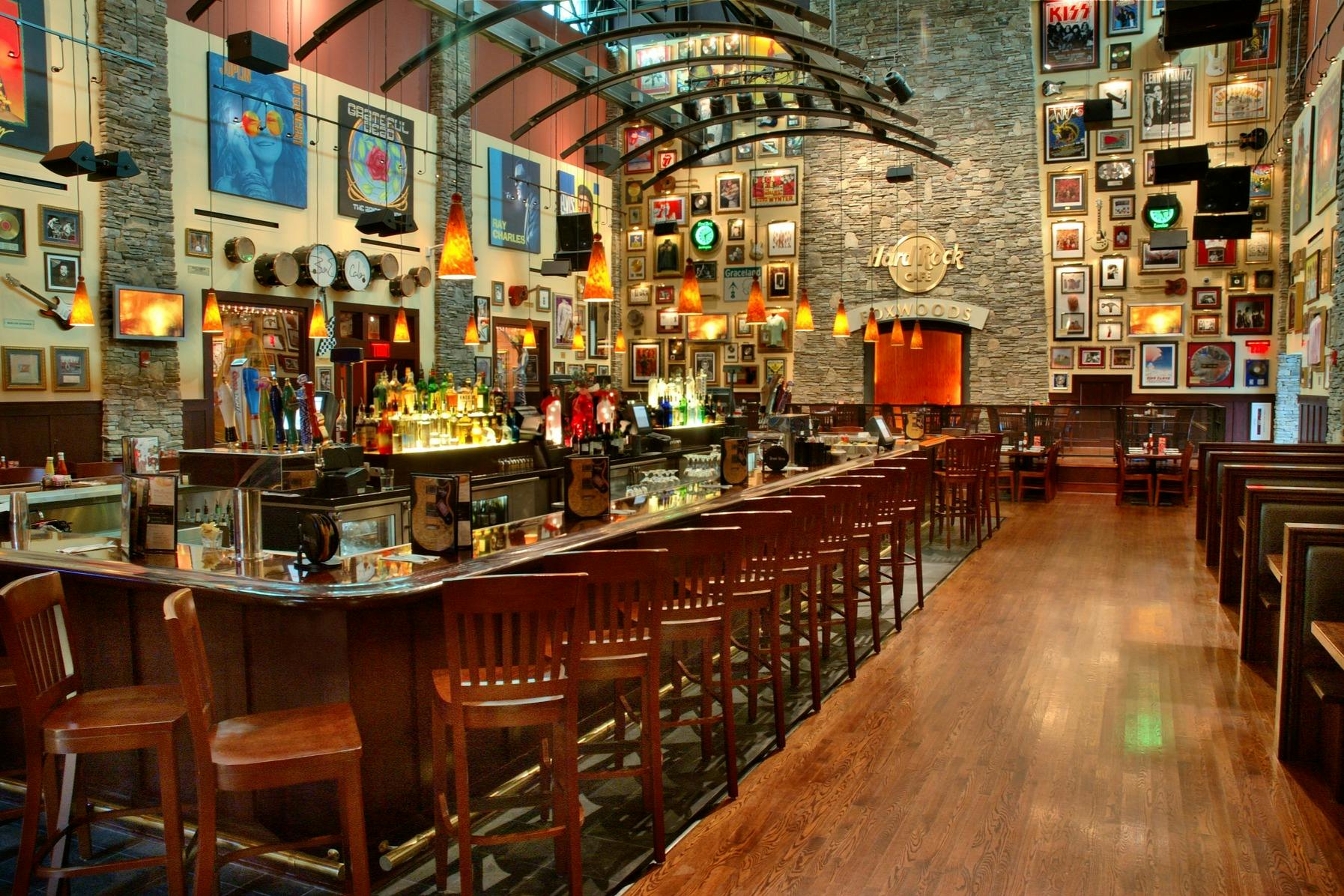 A bar area with high chairs, hanging lights, a variety of drinks, and walls adorned with music memorabilia and framed pictures.