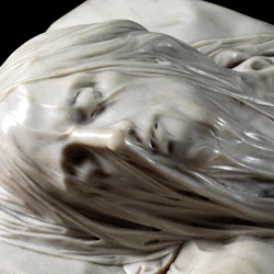 Närbild av en marmorstaty som visar ett fridfullt ansikte med långt hår och slutna ögon.