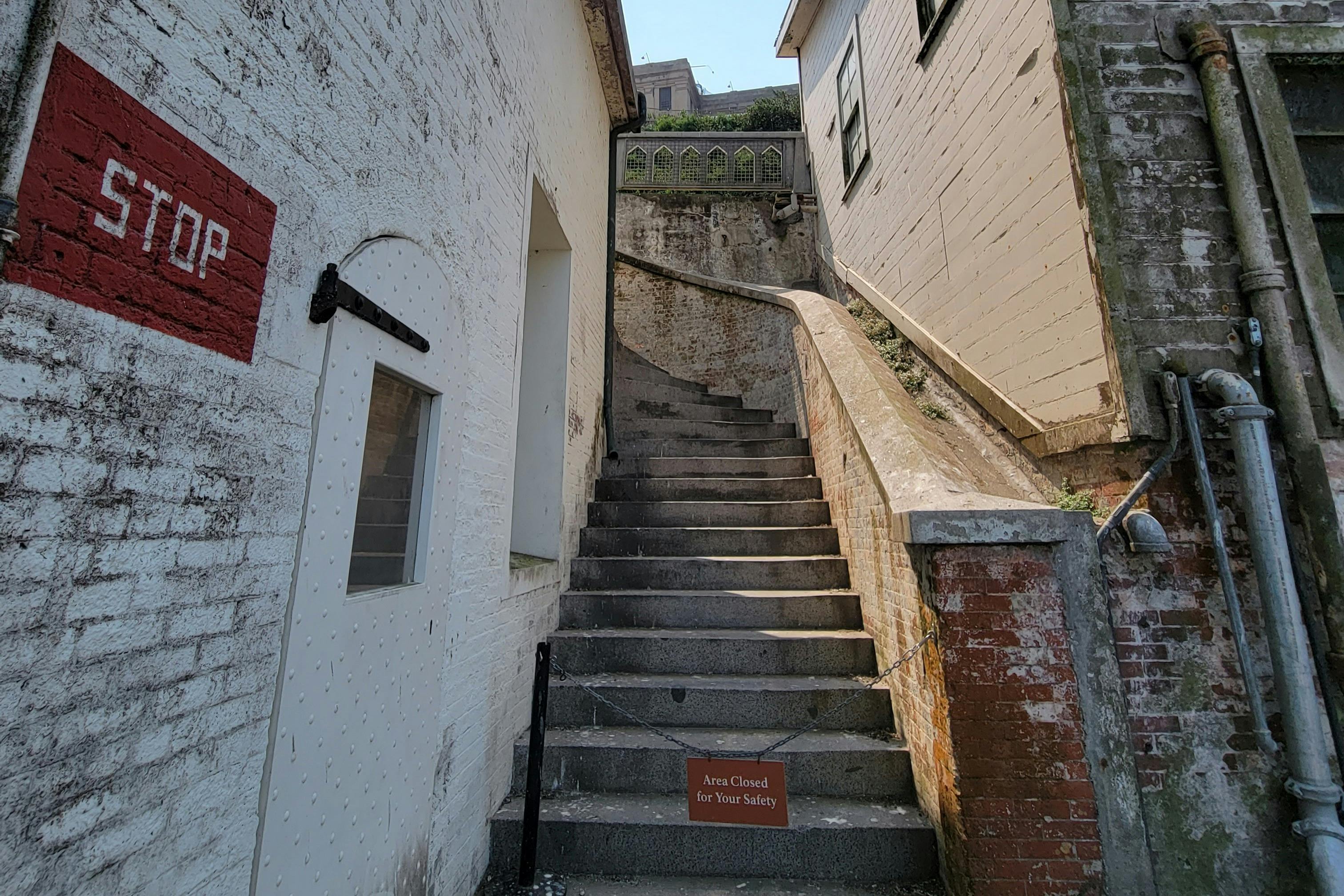 A concrete staircase between two buildings with a sign at the bottom reading "Area Closed for Your Safety."
