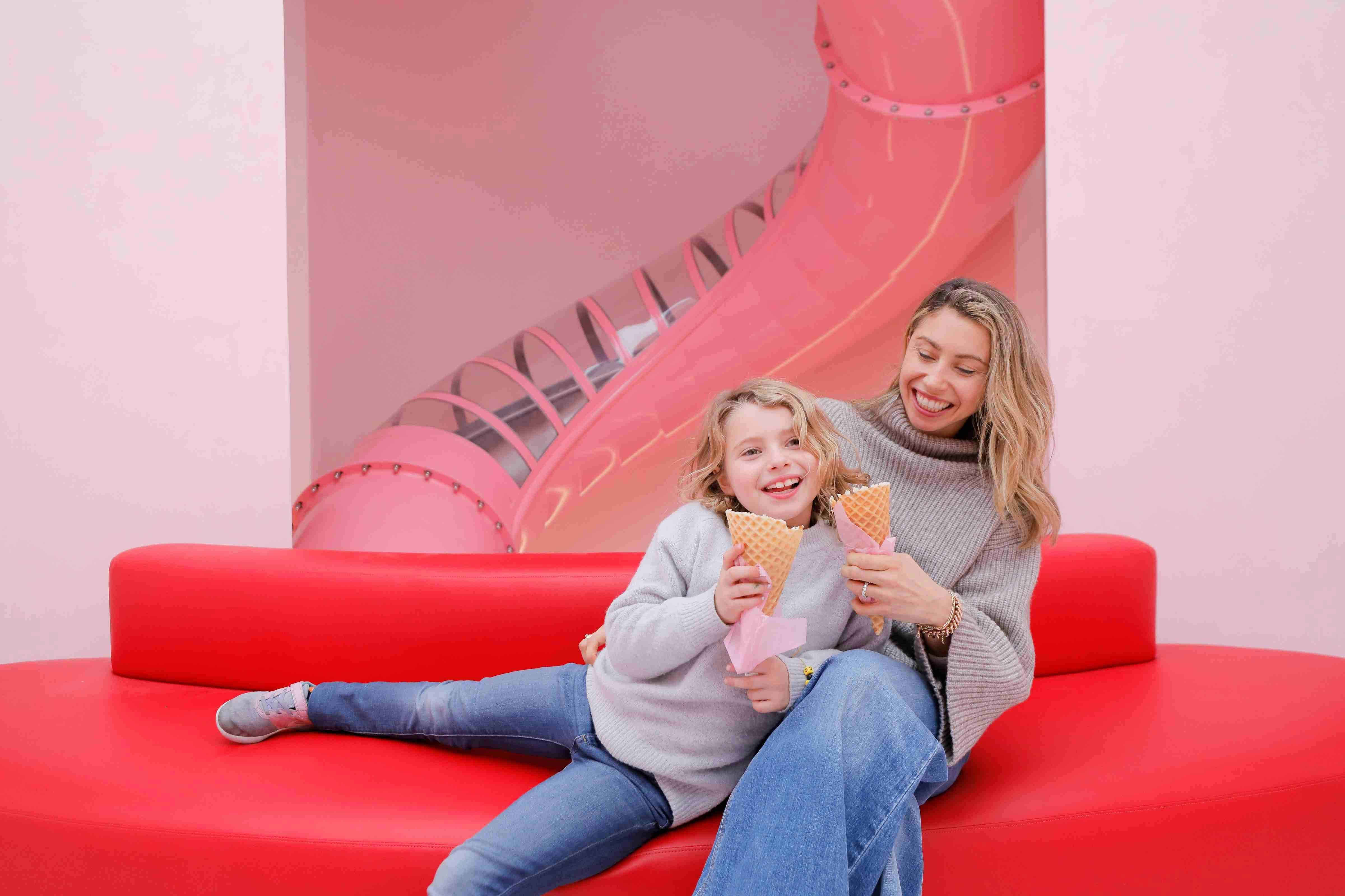 Two people sitting on a red couch eating ice cream cones, with a pink slide in the background.