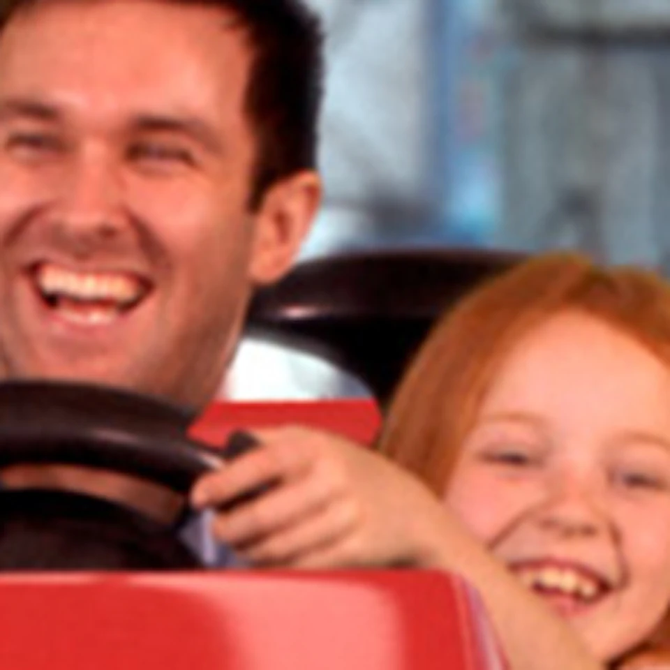 A man and a girl ride in a bumper car themed with an 'Angry Birds' design, both smiling and holding the steering wheel.