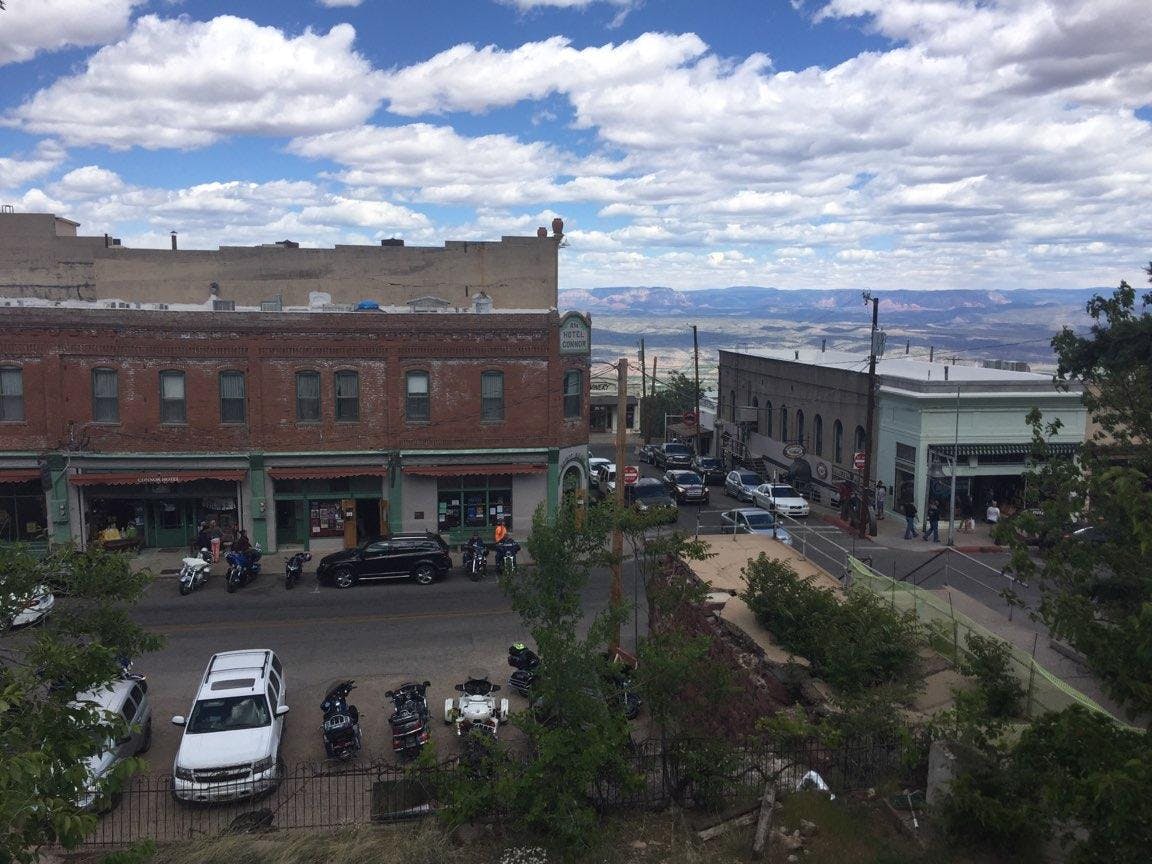 バイク、車、歩いている人が駐車している小さな町の通り。 レンガ造りの建物と風光明媚な風景を背景にしています。