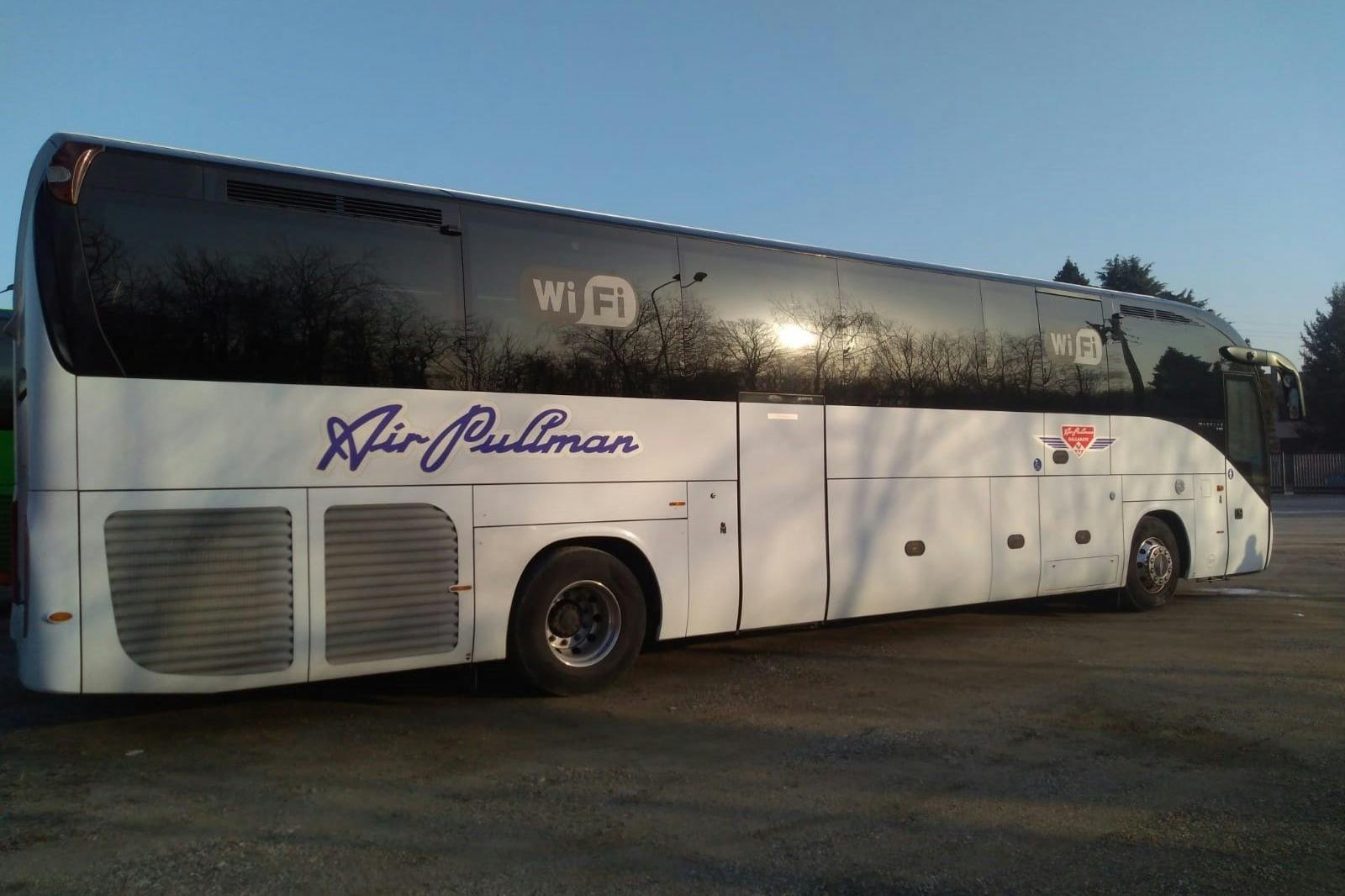 A white "Air Pullman" bus with "WiFi" decal parked on a gravel area under a clear blue sky.