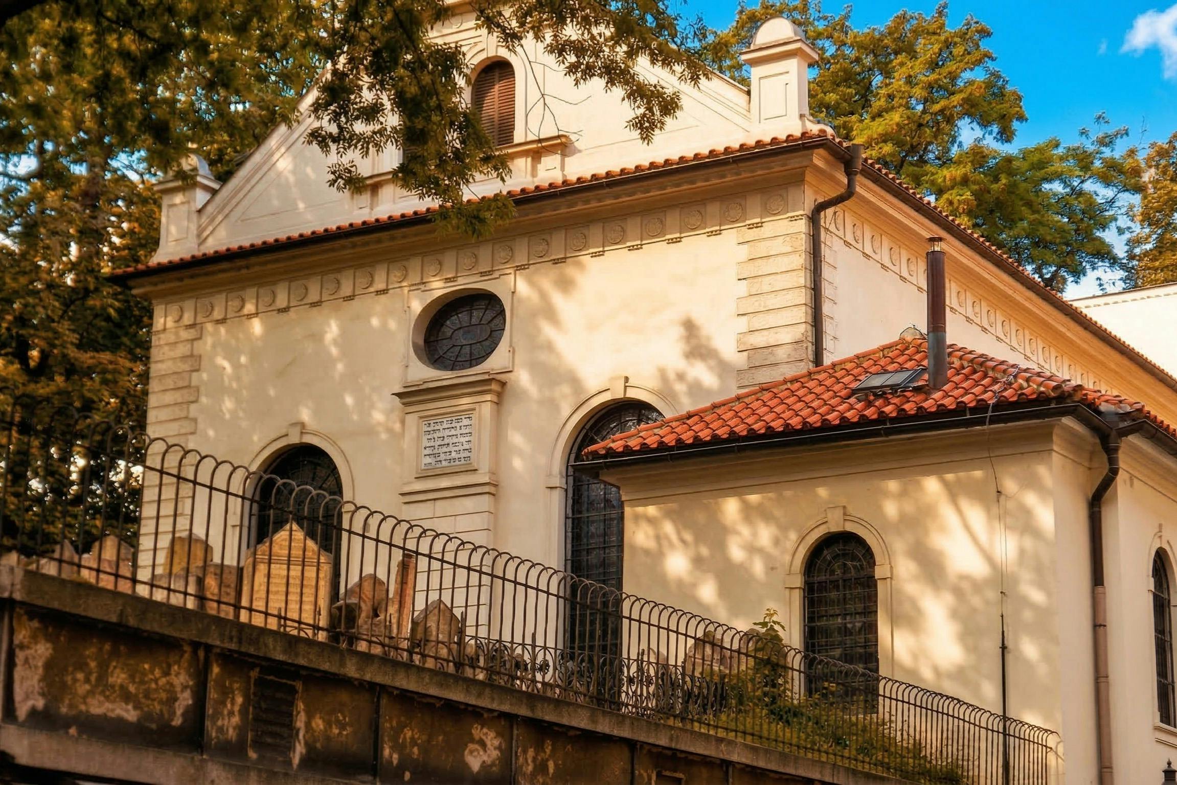 아치형 창문, 붉은 기와 지붕, 금속 울타리로 둘러싸인 작은 묘지가 있는 역사적인 건물입니다.