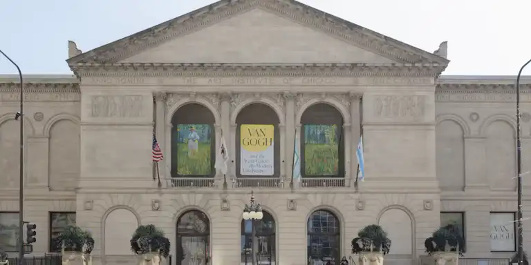 Fasada Art Institute of Chicago, z transparentami na wystawę Van Gogha, flagami i ludźmi przechodzącymi obok.