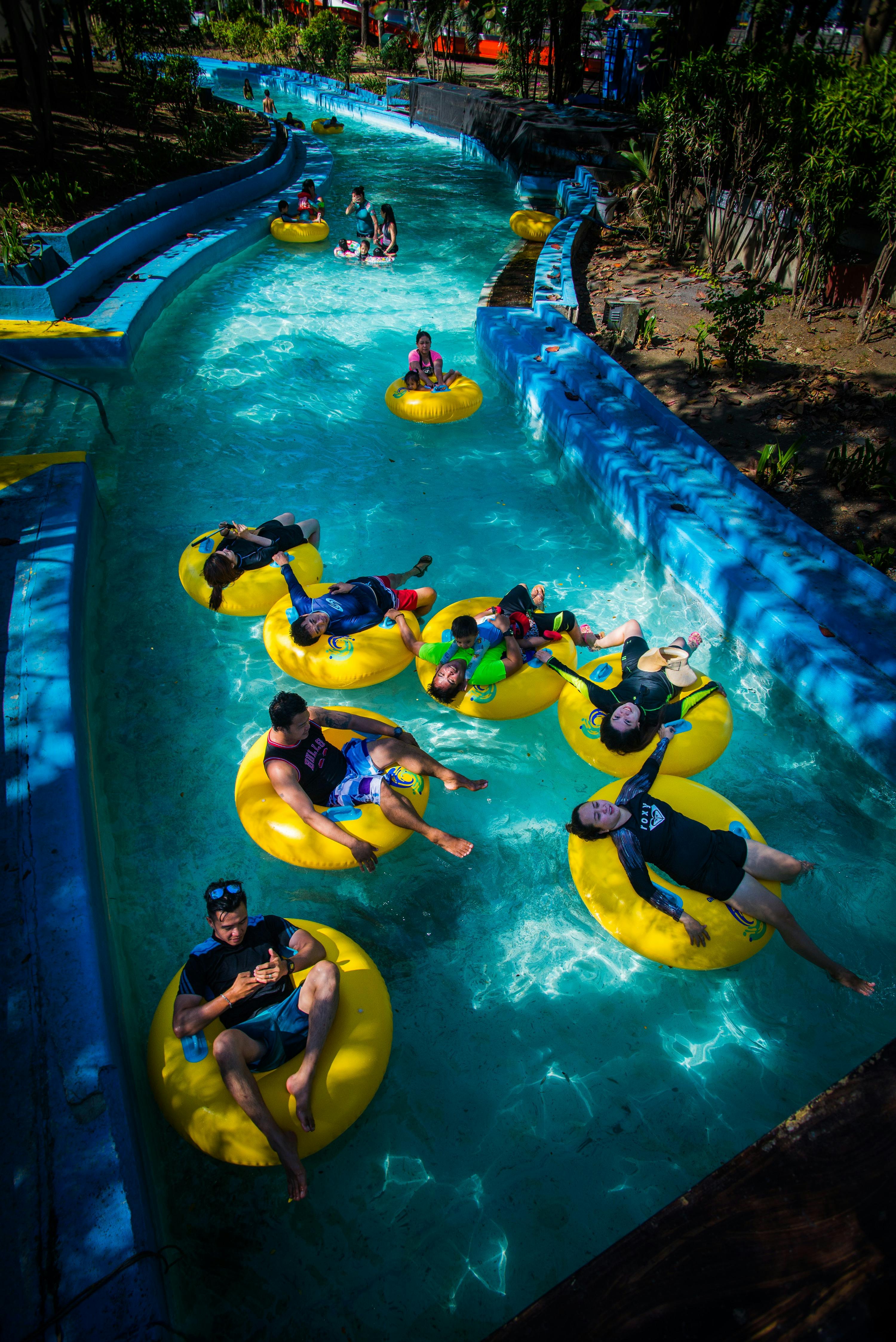 A group of people relaxing on yellow inner tubes in a pool under sunlight and shade.