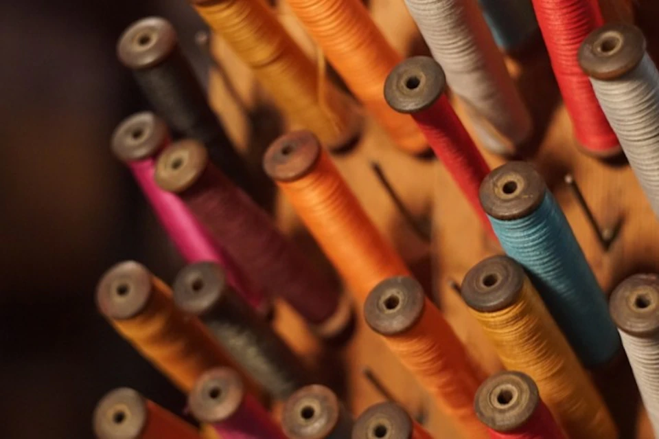 Close-up view of colorful thread spools arranged upright on a wooden rack.