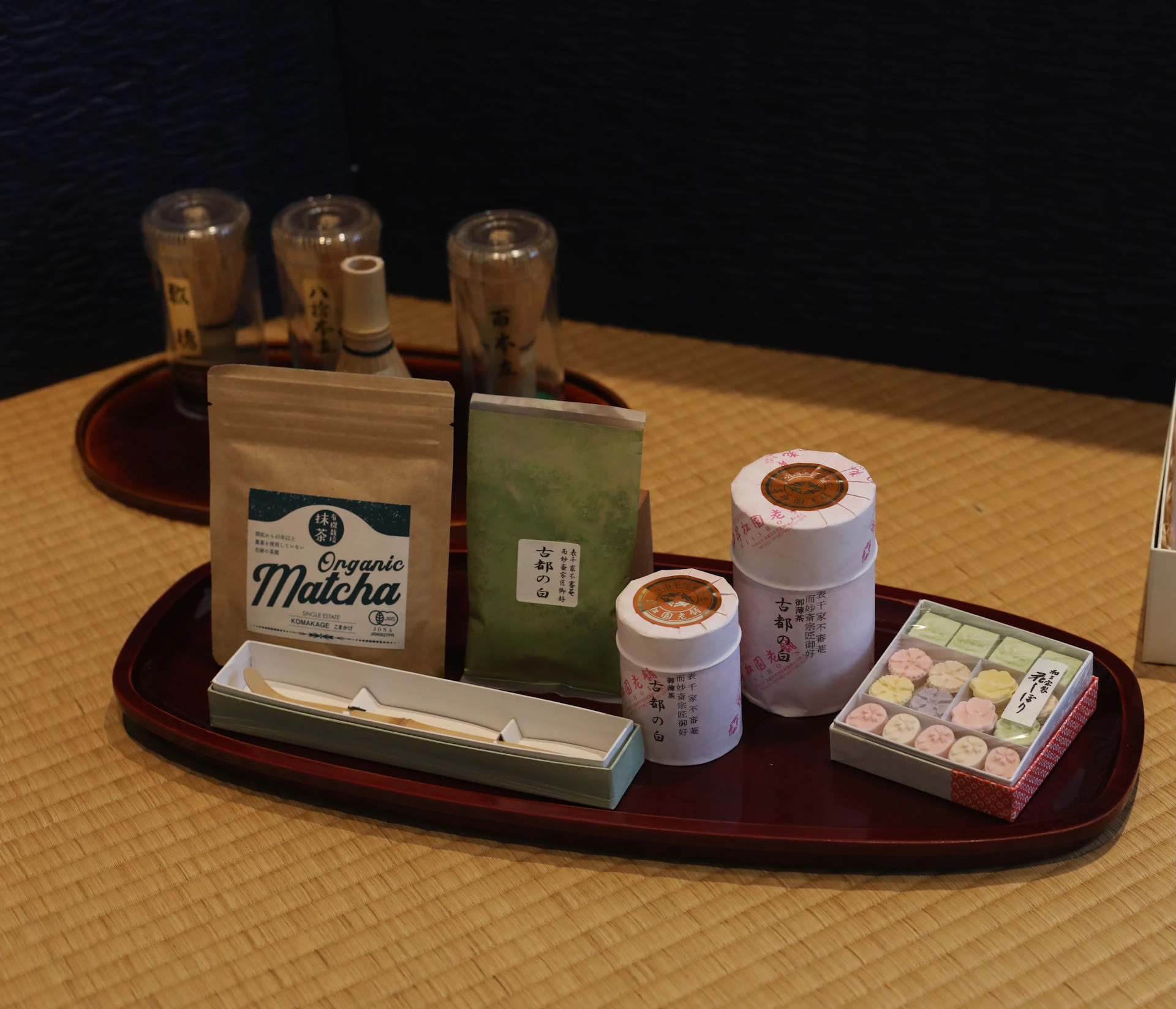 A tray with matcha tea products and accessories, including labeled packets, containers, and a box of sweets.