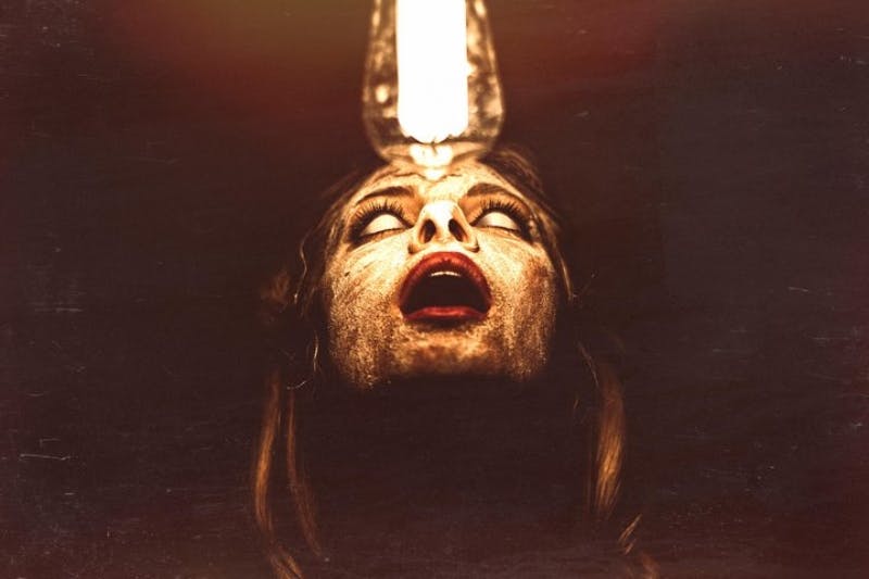 A person with a distressed expression looks upwards towards a bright lightbulb, illuminating their face in a dark setting.