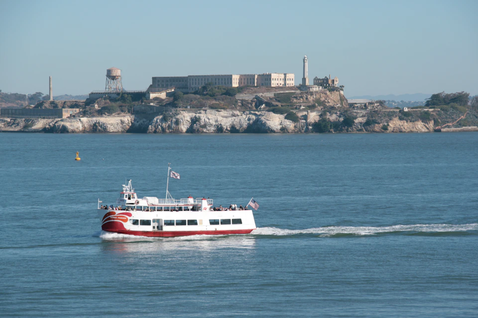 A ferryboat on the water with Alcatraz Island and its buildings in the background on a clear day.