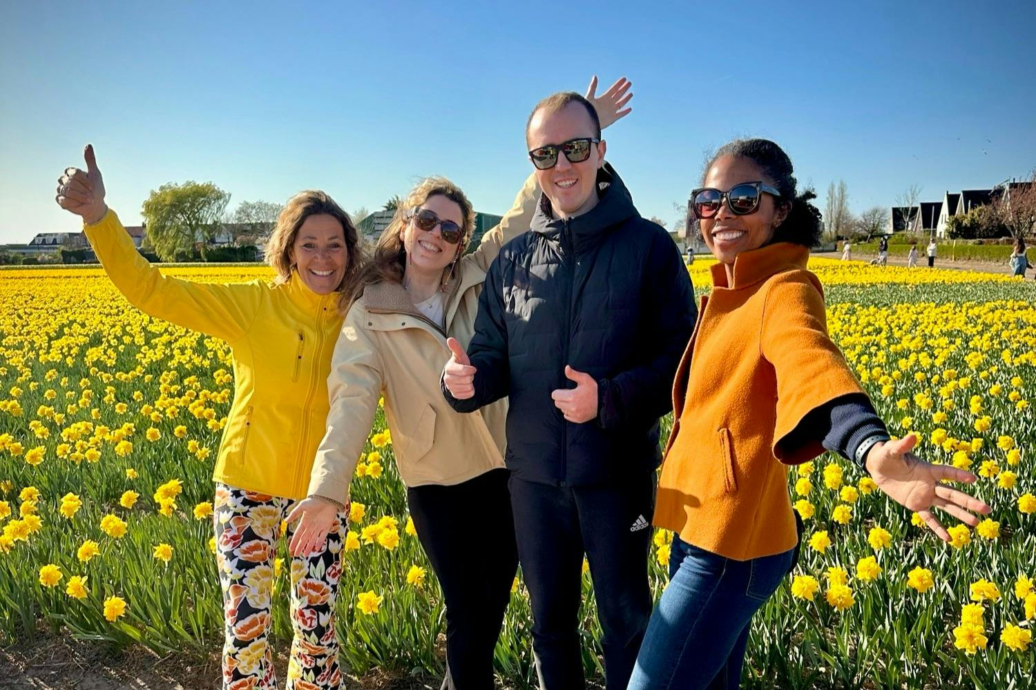 四个人面带微笑，在晴朗的蓝天下的一片黄花中摆姿势。