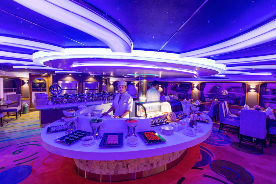 A chef stands behind a circular sushi bar in a restaurant with futuristic blue lighting and curved ceiling designs.