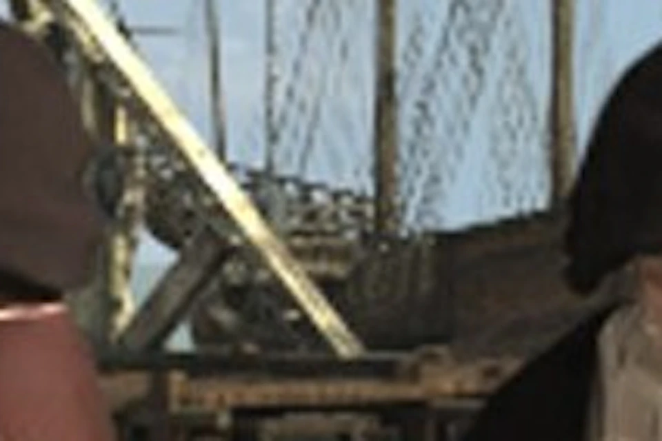 People in medieval attire working near a wooden table with maps, a stone tower, and a large wooden structure in the background.