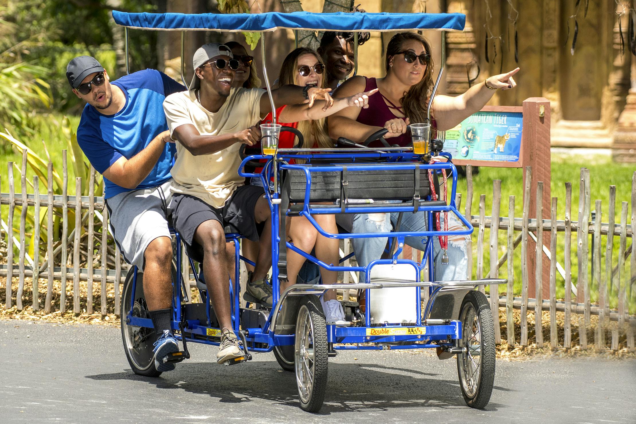 En gruppe mennesker, der kører på en fire-personers pedalcykel med en baldakin, der smiler og peger, mens de nyder deres tur.