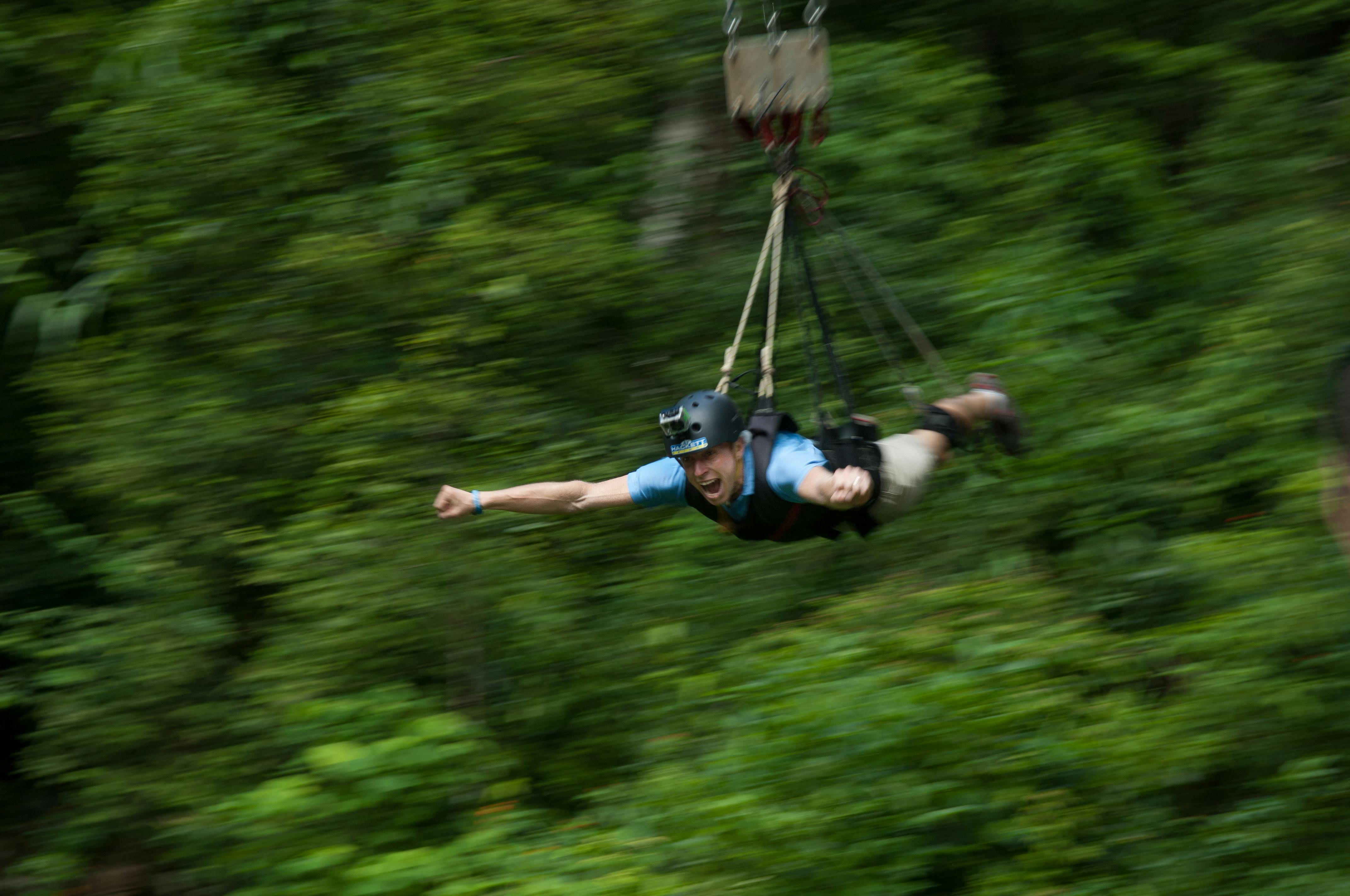 一个穿着蓝色衬衫和头盔的人穿过郁郁葱葱的绿色森林，显得很兴奋，伸出一只胳膊。