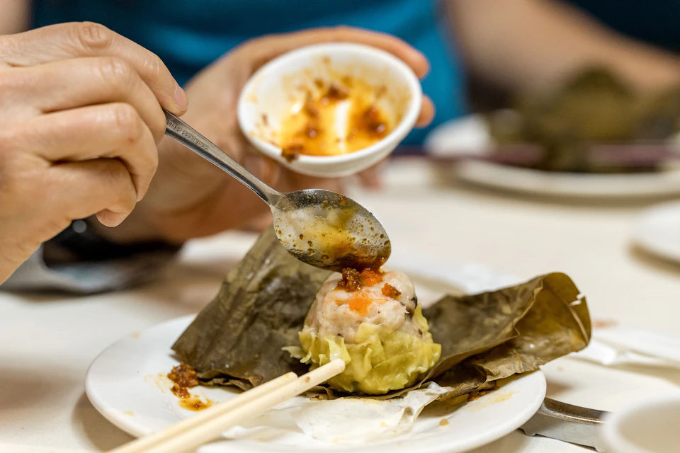 A close up shot of tasty chili oil being scooped and poured on top of a chinese dumpling