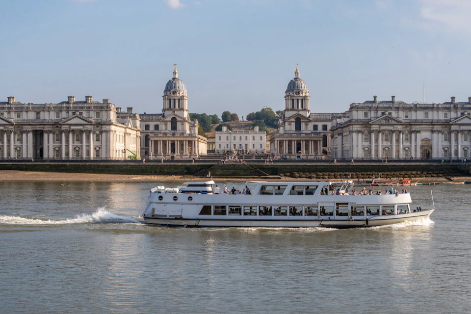 A white passenger boat on a river with a historic building featuring domed towers in the background.