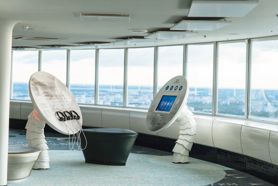 Modern indoor observation deck with a view of the city through large windows, featuring interactive exhibits and seating.