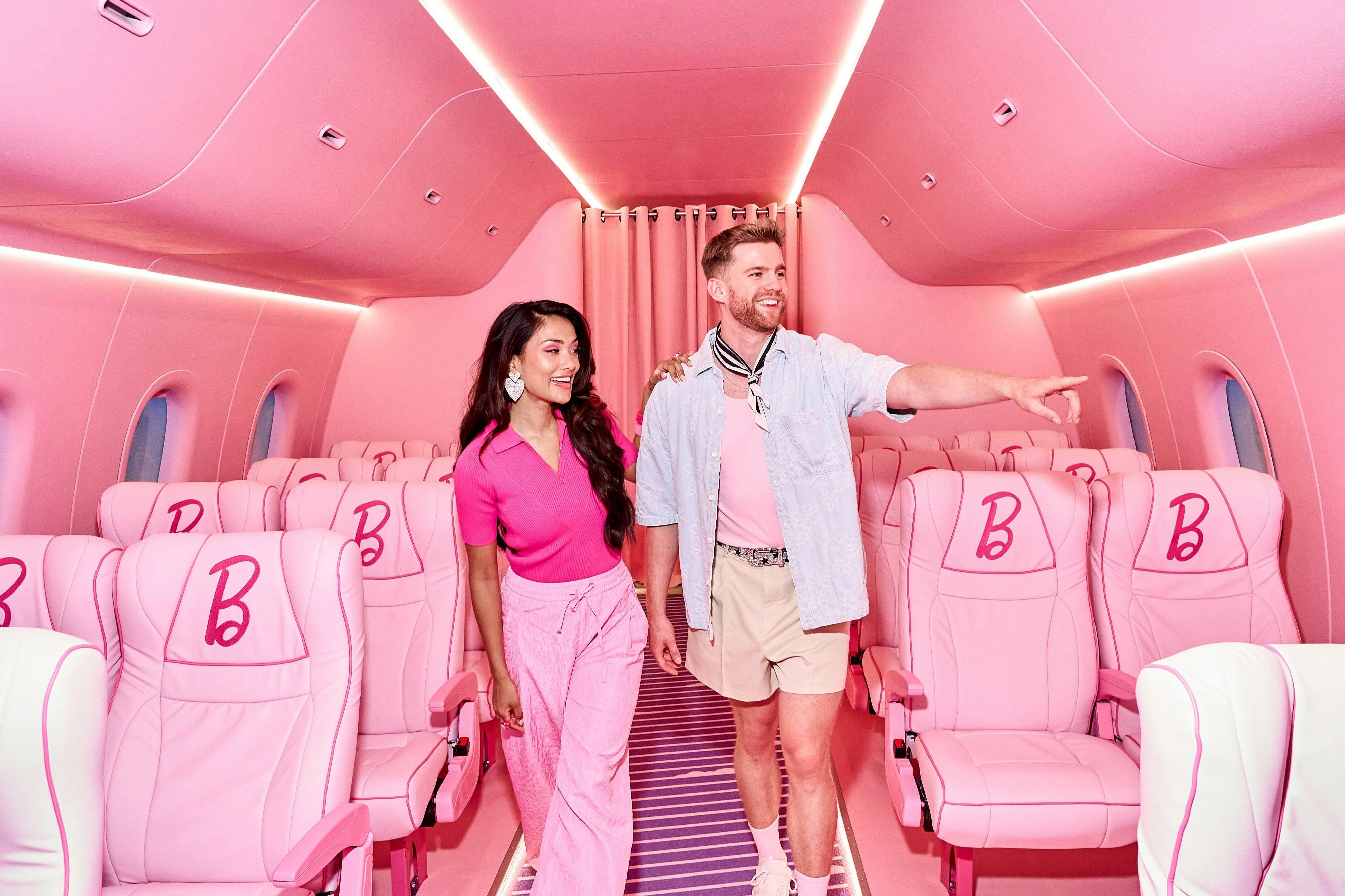 Dva lidé kráčející v růžové kabině letadla s logy „B“ na růžových sedadlech; muž ukazuje dopředu.