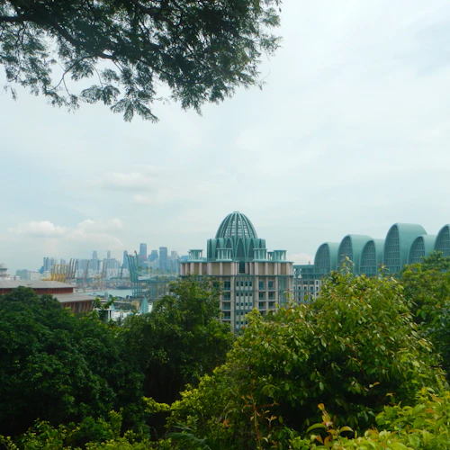 Moderne Stadtsilhouette mit einzigartigen Gebäuden mit grünen Dächern, umgeben von Bäumen, unter einem bewölkten blauen Himmel.