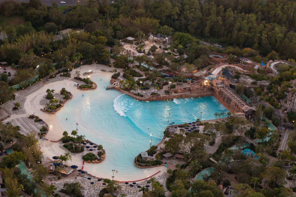 Aerial view of a large water park with a wave pool, surrounded by greenery, walkways, and various water attractions.