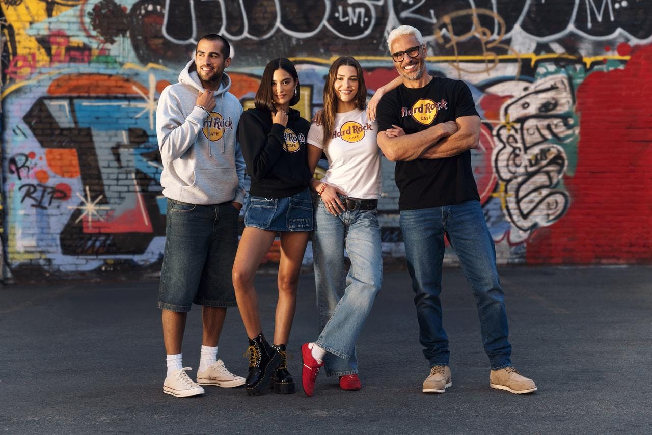 Four people wearing Hard Rock Cafe shirts posing in front of a graffitied wall, smiling and standing closely together.