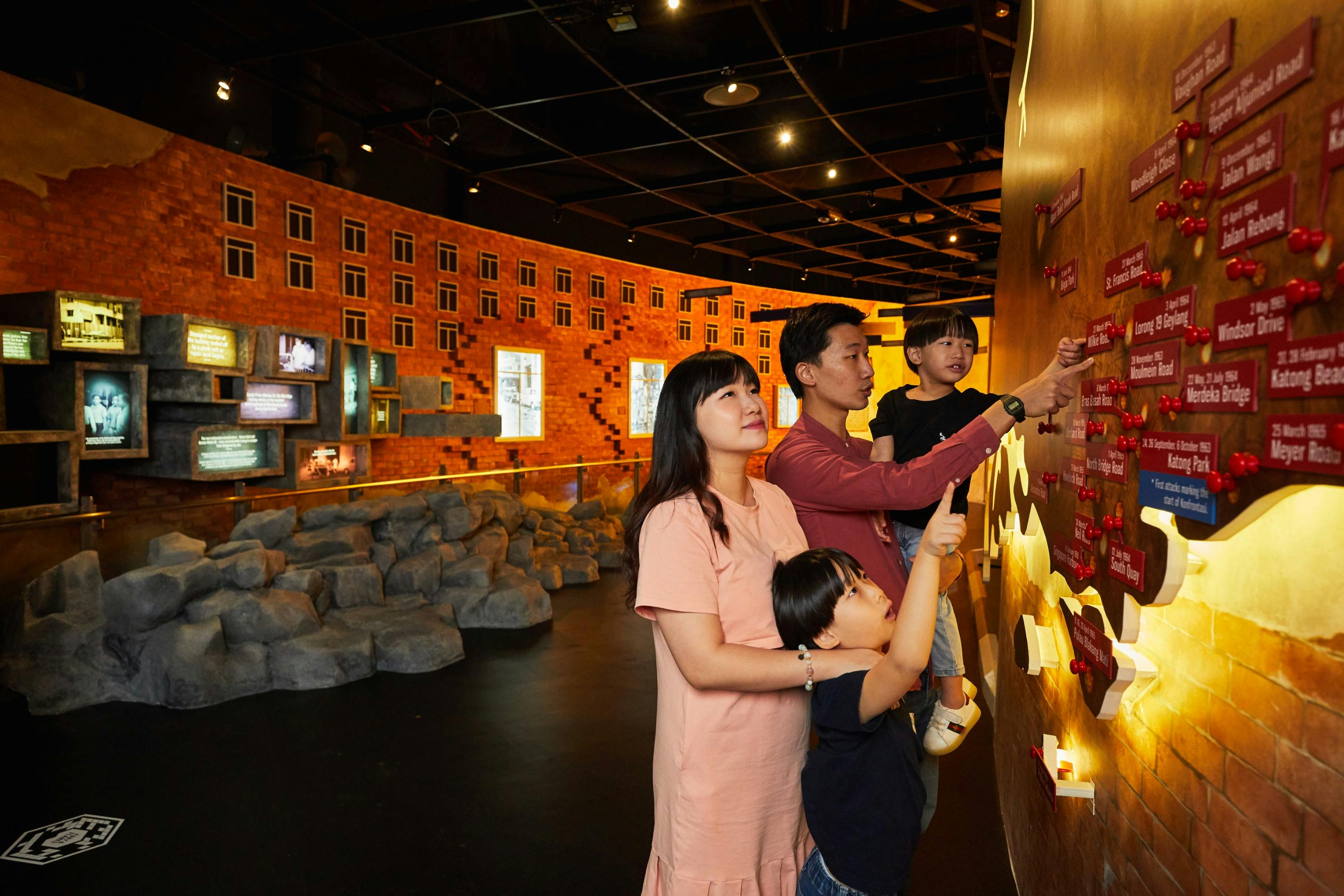 A family of four interacts with an illuminated wall display in a museum-like setting with a brick-themed interior.