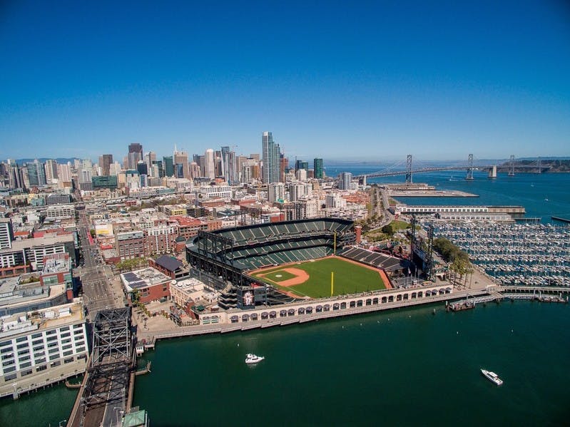 고층 건물과 다리를 배경으로 한 도시의 수변 야구 경기장의 공중 전경.