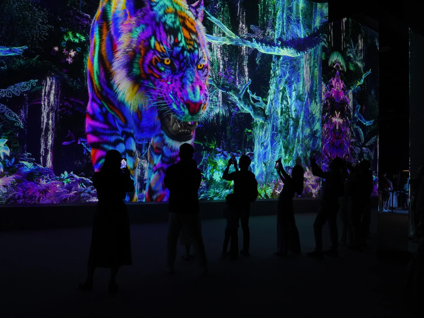 A group of people silhouetted in front of a vibrant digital display featuring a multicolored tiger in a jungle scene.