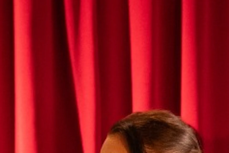 A man and woman in period costumes perform in front of a red curtain, while seated diners watch in an ornate setting.