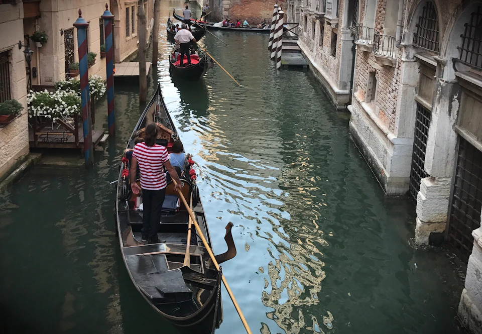 Gondoliers navigating traditional boats with passengers through a narrow canal between historic buildings in Venice.