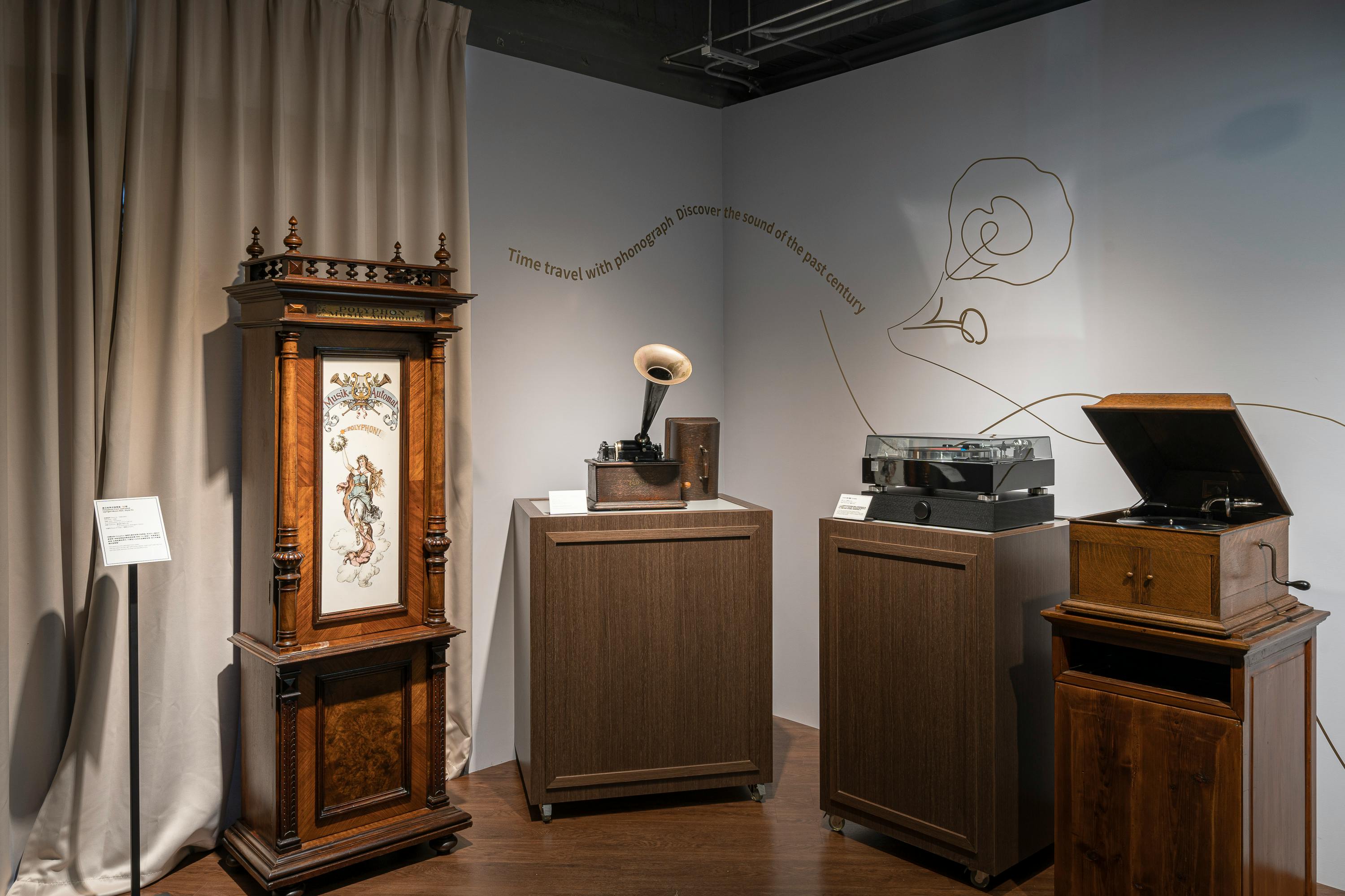 A display of vintage phonographs and a decorative cabinet in a museum setting with wall text about sound history.