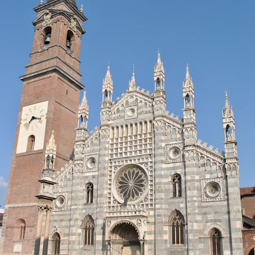 En gotisk katedral med ett högt klocktorn, invecklad fasad, dekorativa spiror och människor som går i närheten under en klarblå himmel.