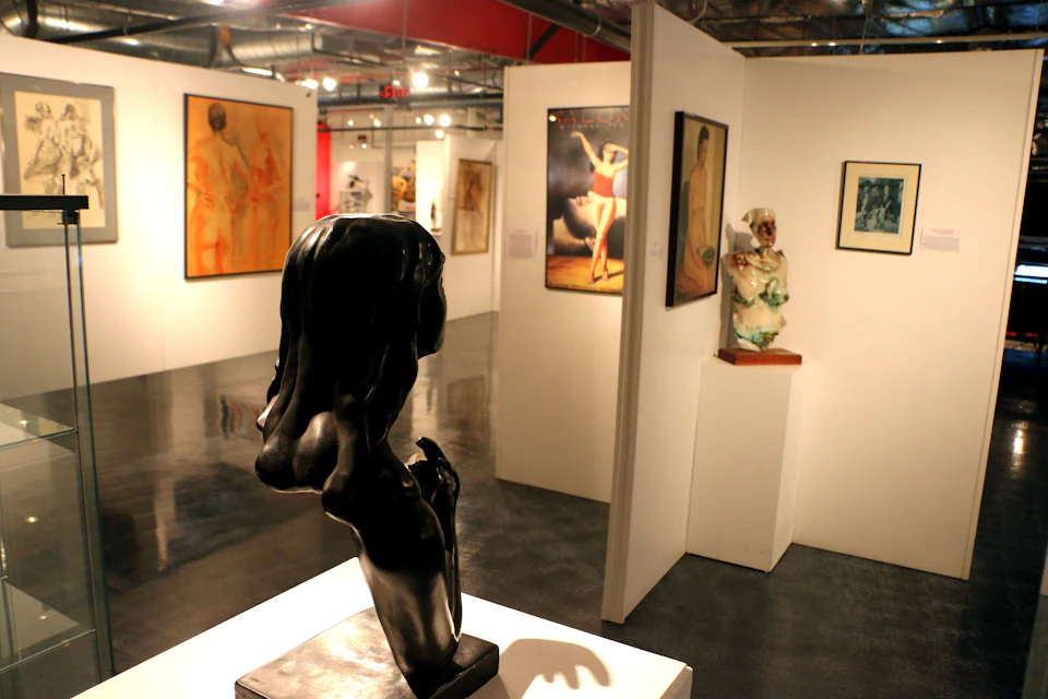 Art gallery with sculptures and paintings, including a black abstract sculpture in the foreground and various artworks on white walls.