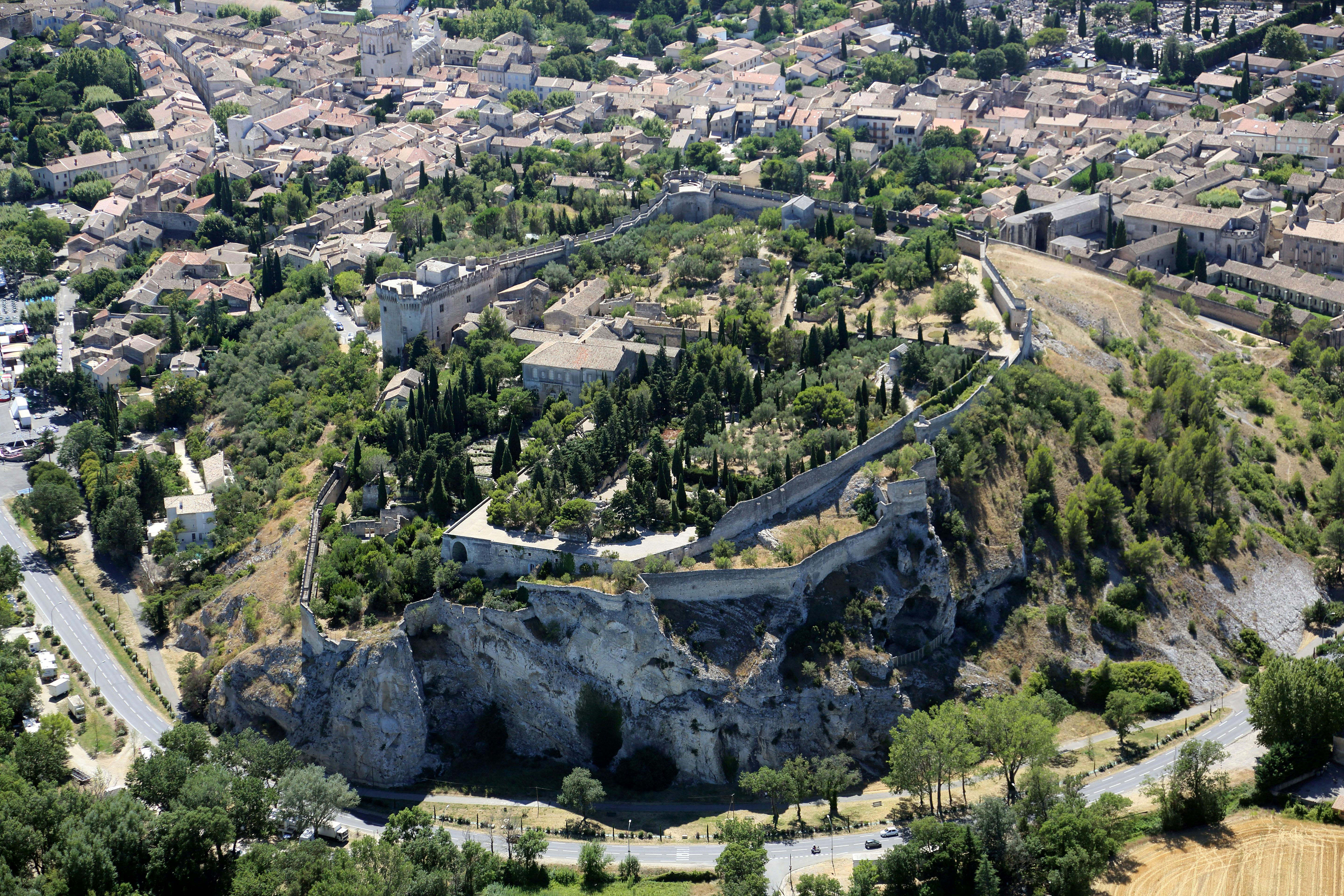 鸟瞰历史悠久的防御工事小镇，石墙、茂密的绿色植物和周围的现代建筑。