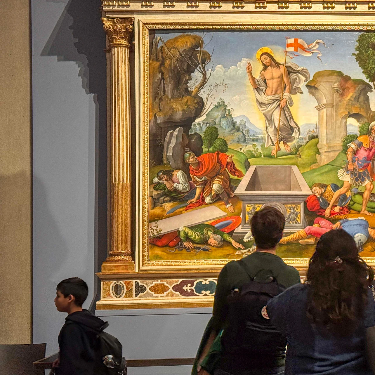 Visitors viewing a Renaissance painting depicting the resurrection of Jesus, displayed in a museum setting.